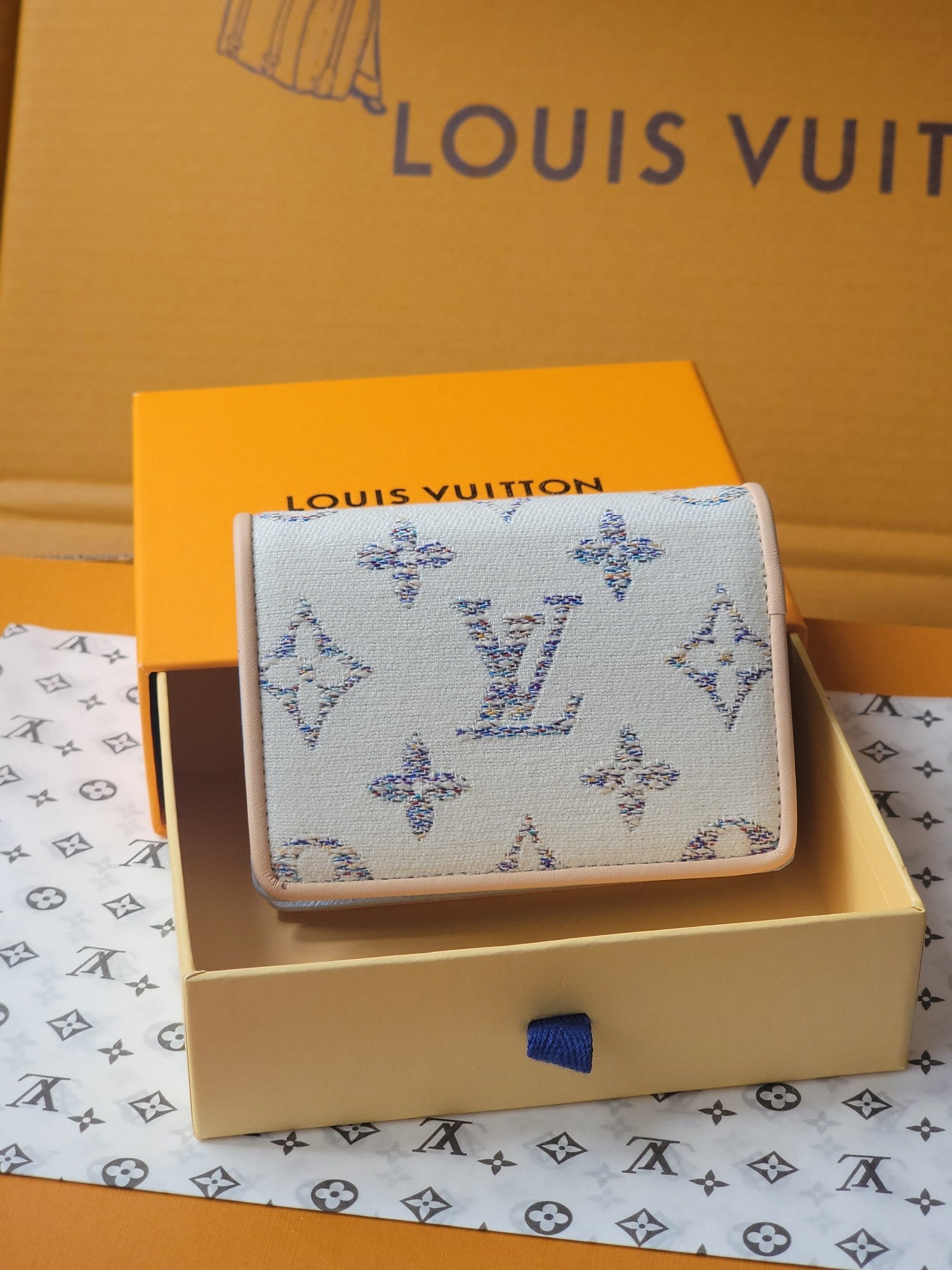 Light blue mini wallet with blue patterned exterior and foldover front in a box