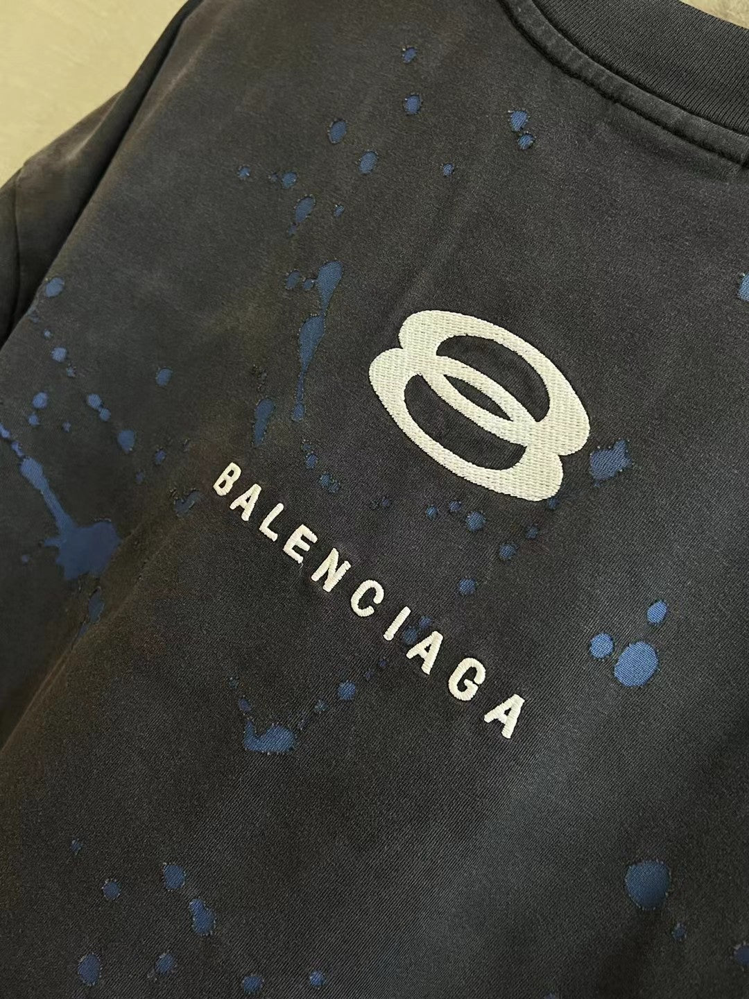 Balenciaga short-sleeve T-shirt logo close-up, dark charcoal with blue splatter and BALENCIAGA letters