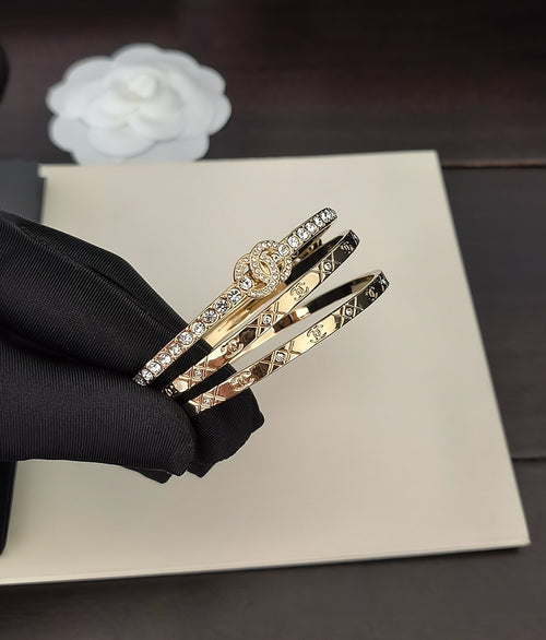 Gold-tone stacked bangles with crystal trim, shown in a black-gloved hand