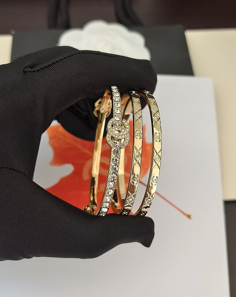 Gold-tone bangle set with crystal medallion detail, held in a black-gloved hand