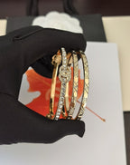 Gold-tone bangle set with crystal medallion detail, held in a black-gloved hand