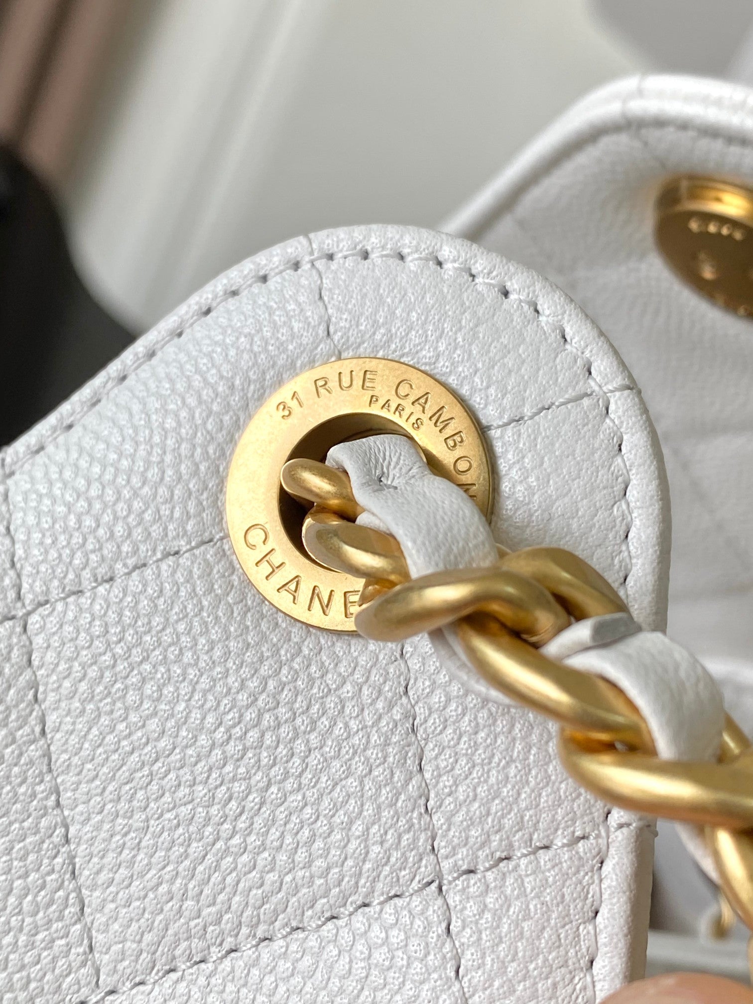 White leather bag with round gold-tone logo and interlocking chain detail