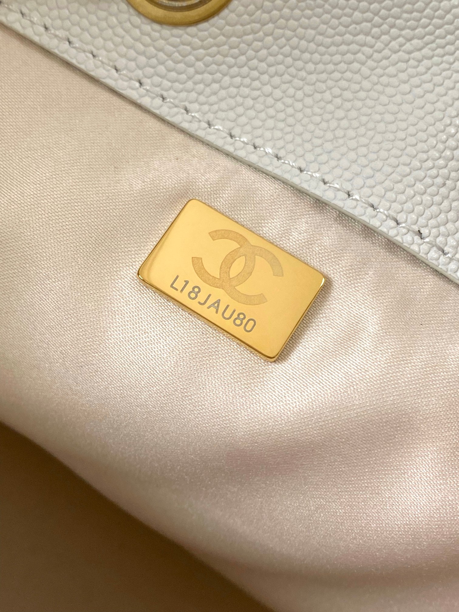 Gold rectangular authenticity tag with Chanel emblem on cream leather bag