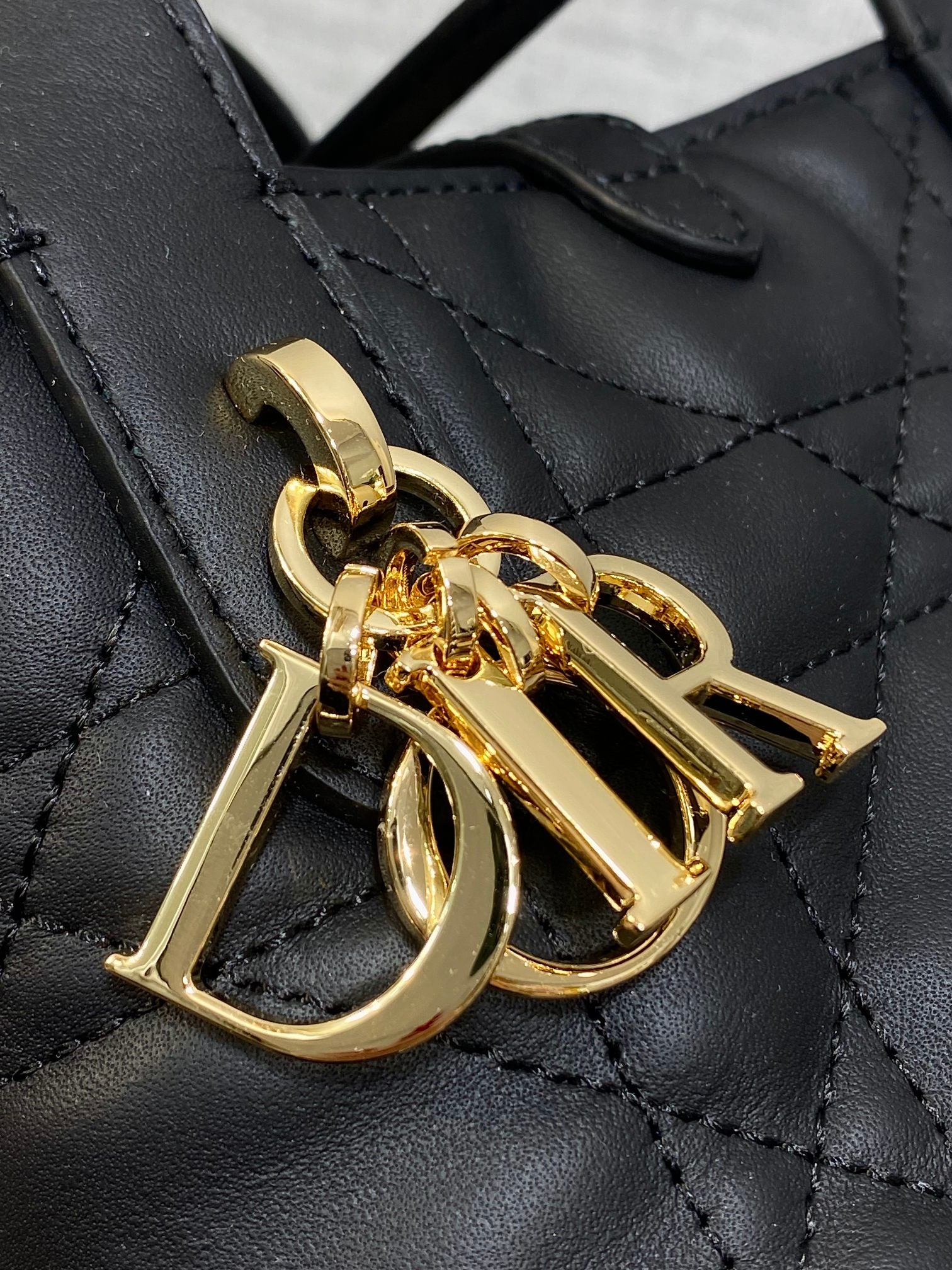 Gold-tone Dior logo charm on black quilted leather tote bag hardware