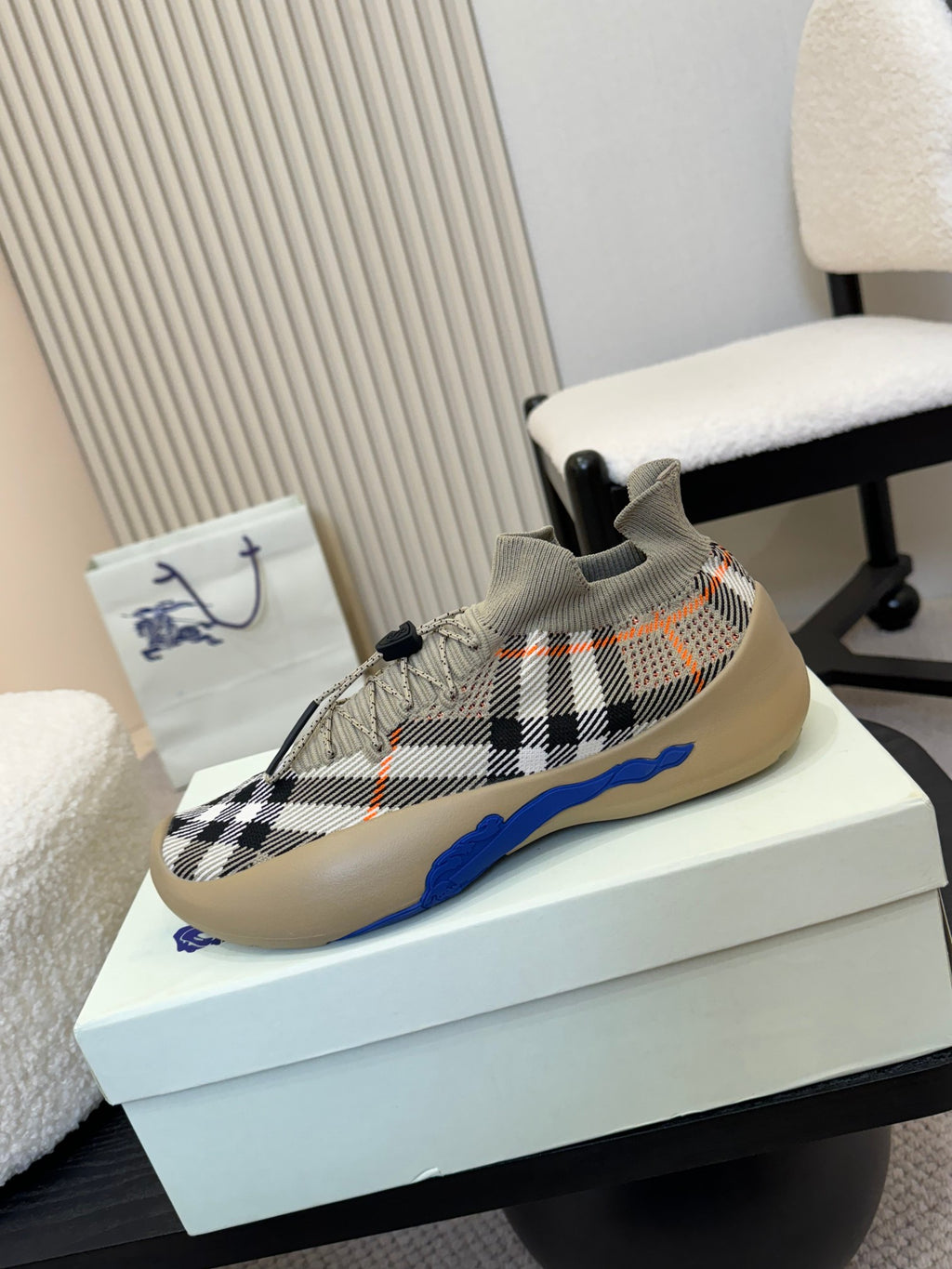 Low-top knit sneaker with black check pattern, orange stitching marks, and blue outsole.