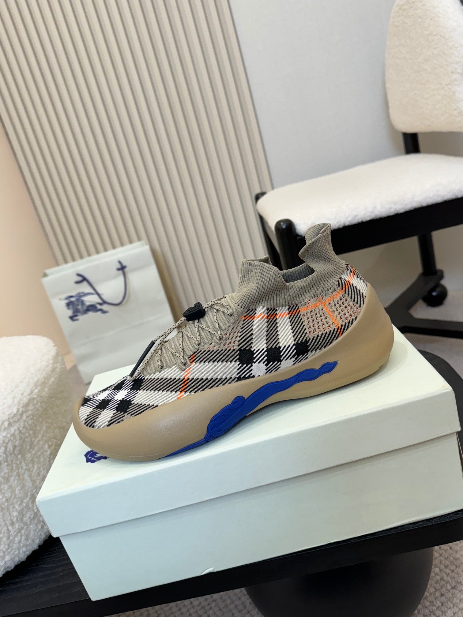 Low-top knit sneaker with black check pattern, orange stitching marks, and blue outsole.