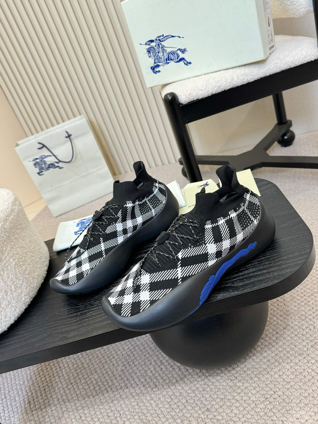 Black knit slip-on sneakers with white check pattern and blue trim on soles