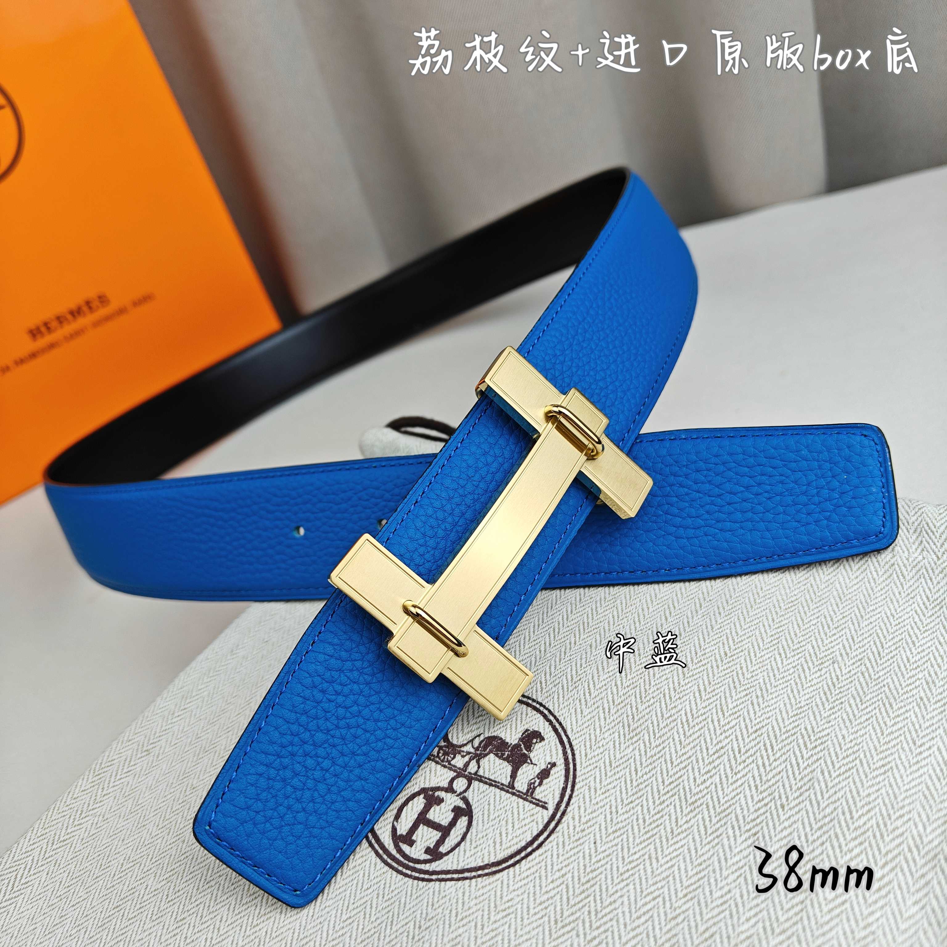 Blue leather Hermes belt with gold buckle, angled view on fabric.