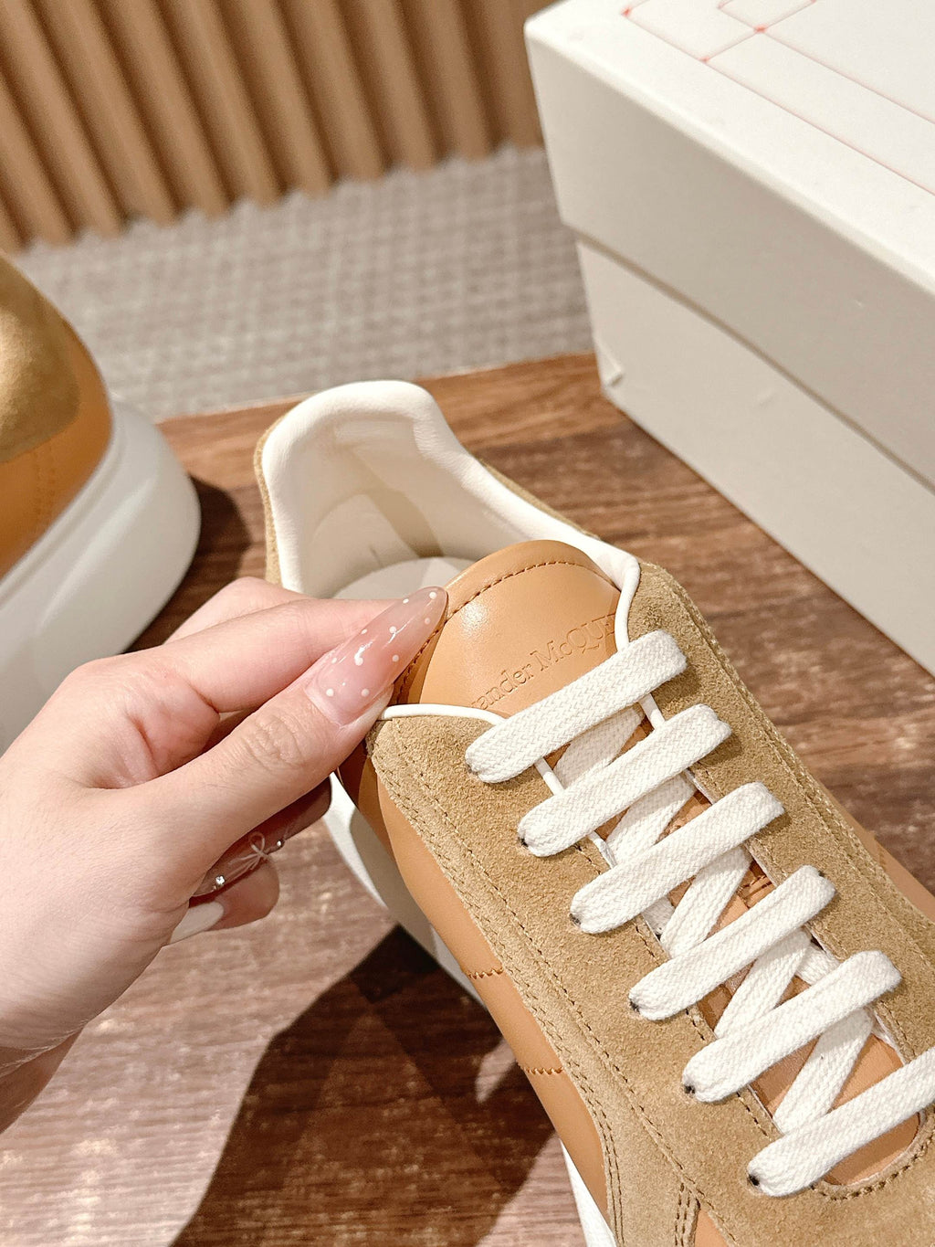 Tan and beige low-top sneaker held in a hand, with white laces and padded collar