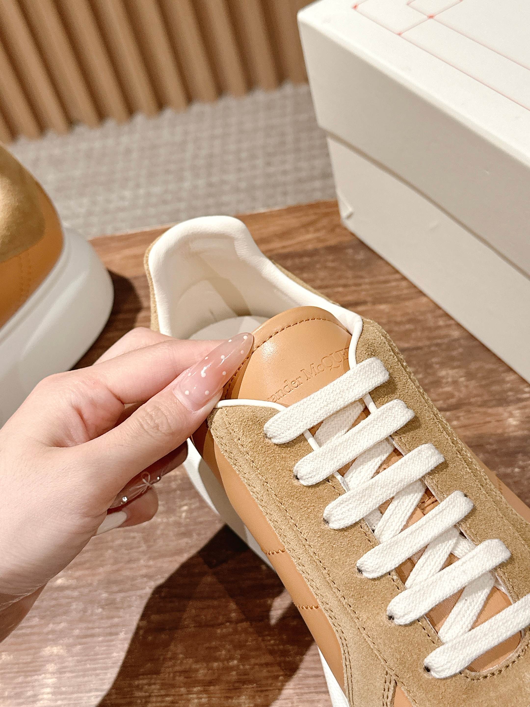 Tan and beige low-top sneaker held in a hand, with white laces and padded collar