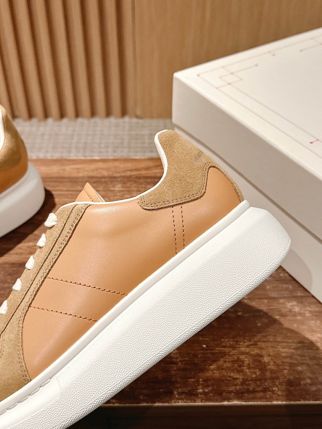 Close-up of tan and beige sneaker with suede panel, white laces, and white sole