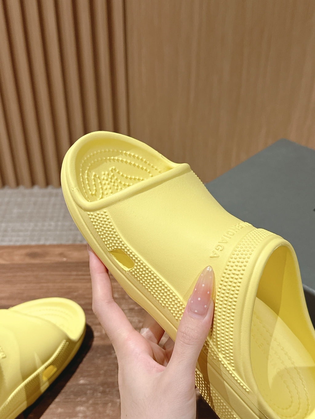Balenciaga yellow slide sandals with textured sole, hand holding one pair