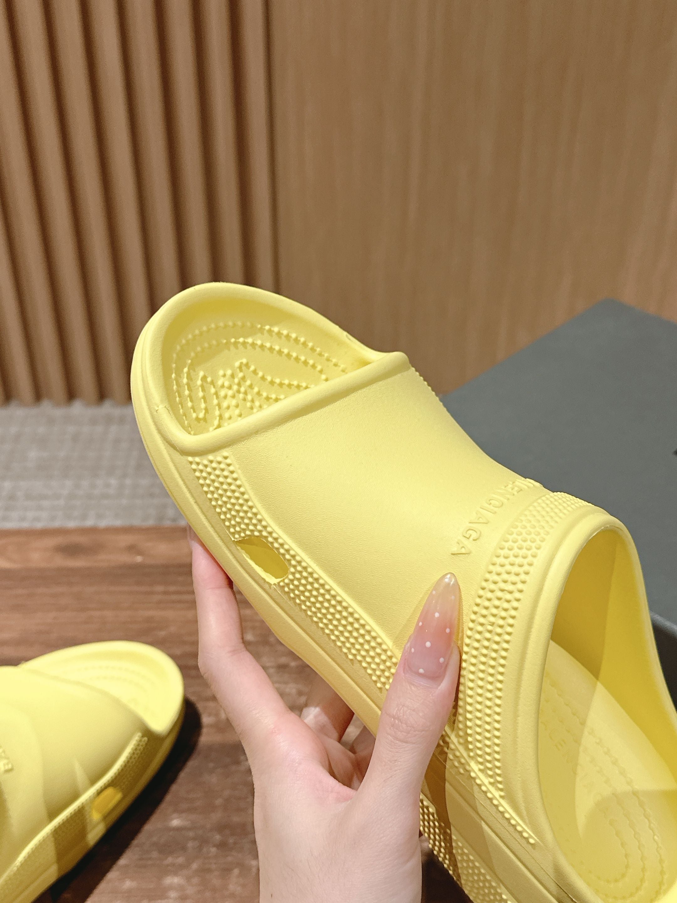 Balenciaga yellow slide sandals with textured sole, hand holding one pair