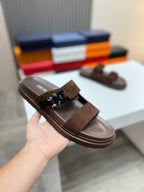 Brown Dior slide sandals held in hand; suede strap with metal buckle