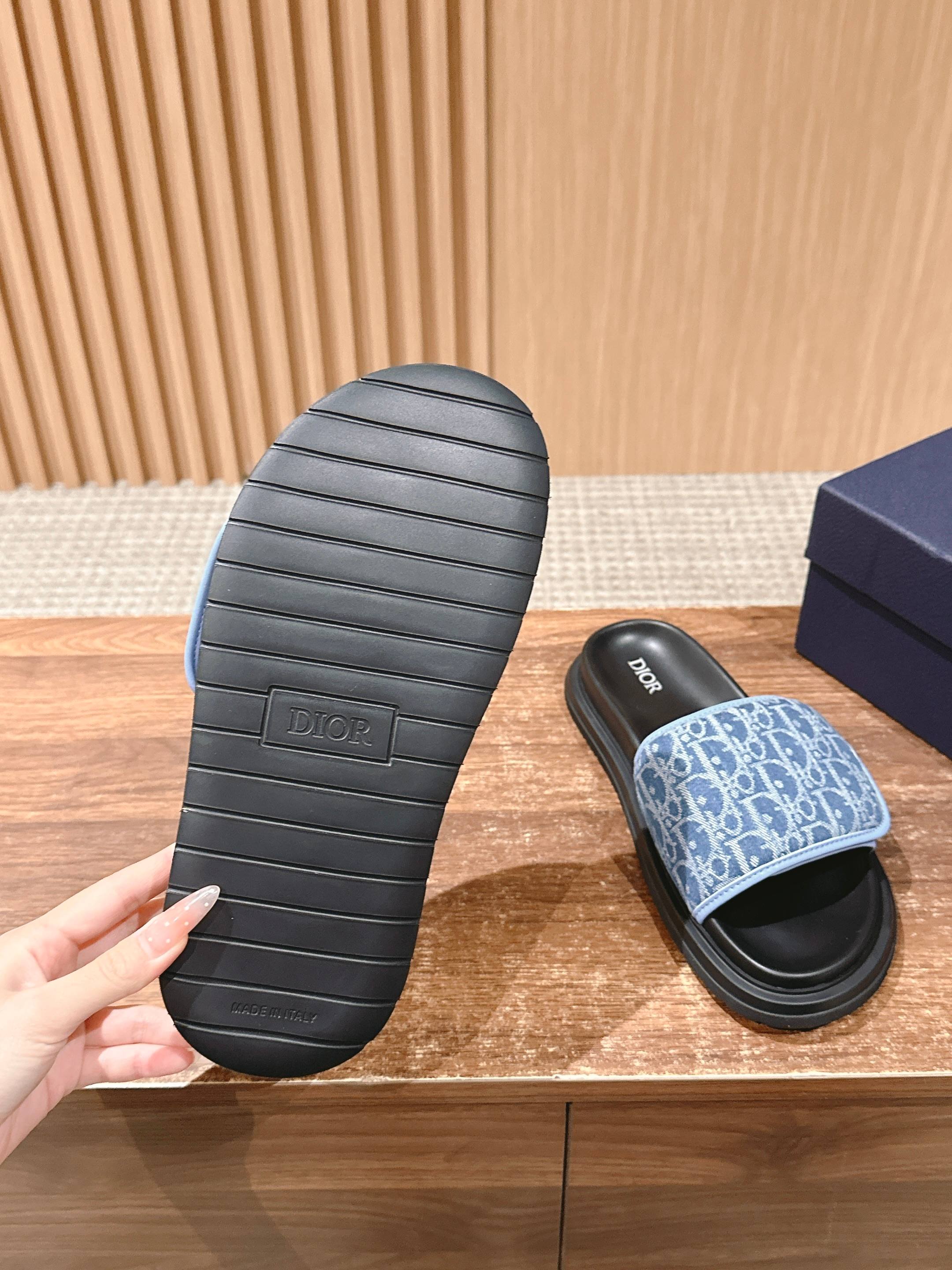 Treaded sole of a black slide sandal next to a blue monogram sandal