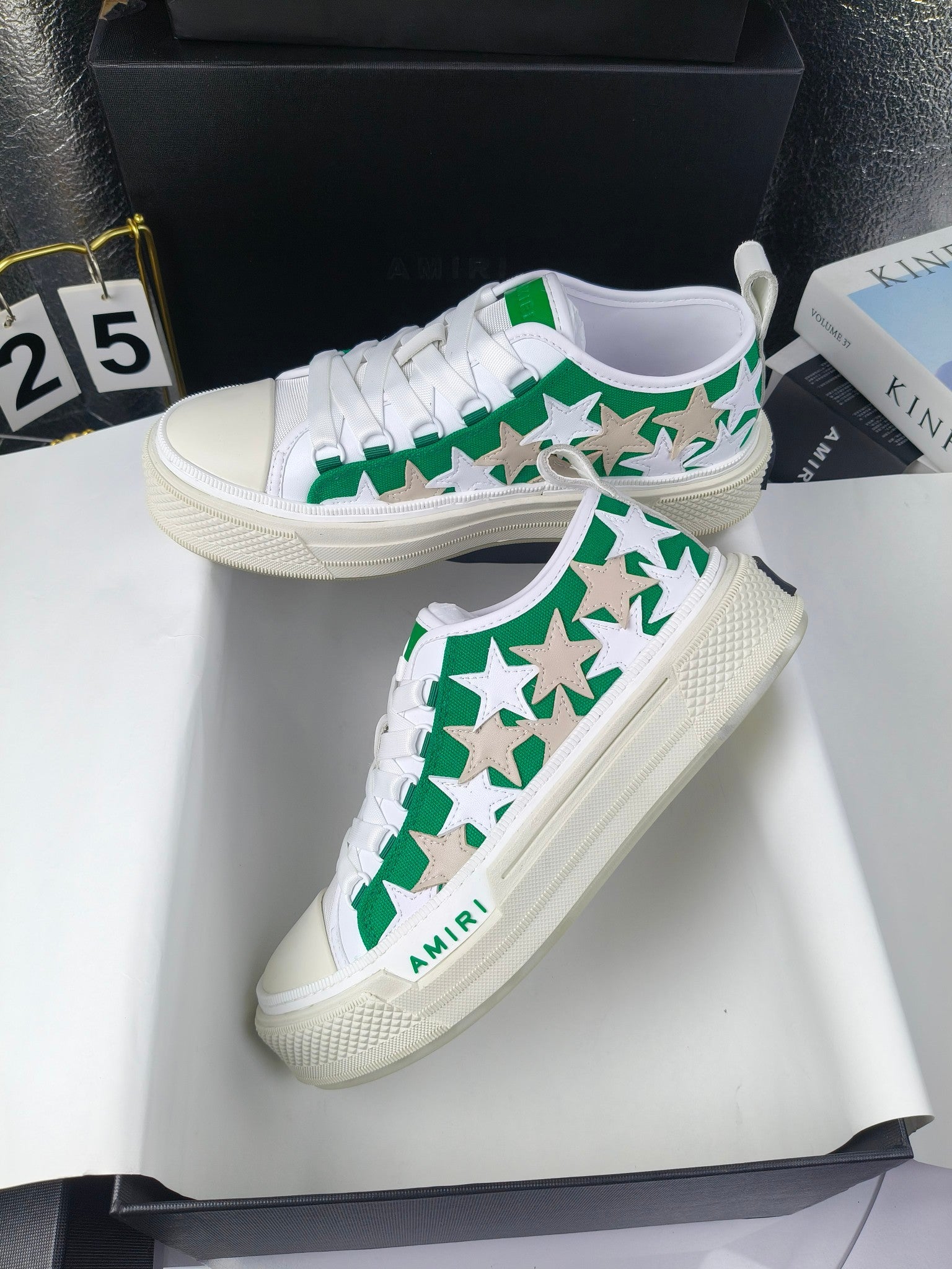 Two white low-top sneakers with green star motif and white laces on display, Amiri