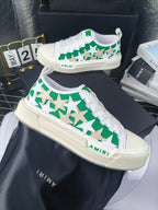 White low-top sneakers with green star motif and white laces, Amiri logo detail