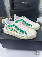 White low-top sneakers with green star motif and white laces, Amiri logo on sole