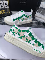 White low-top sneakers with green star pattern, white laces, Amiri branding, angled view