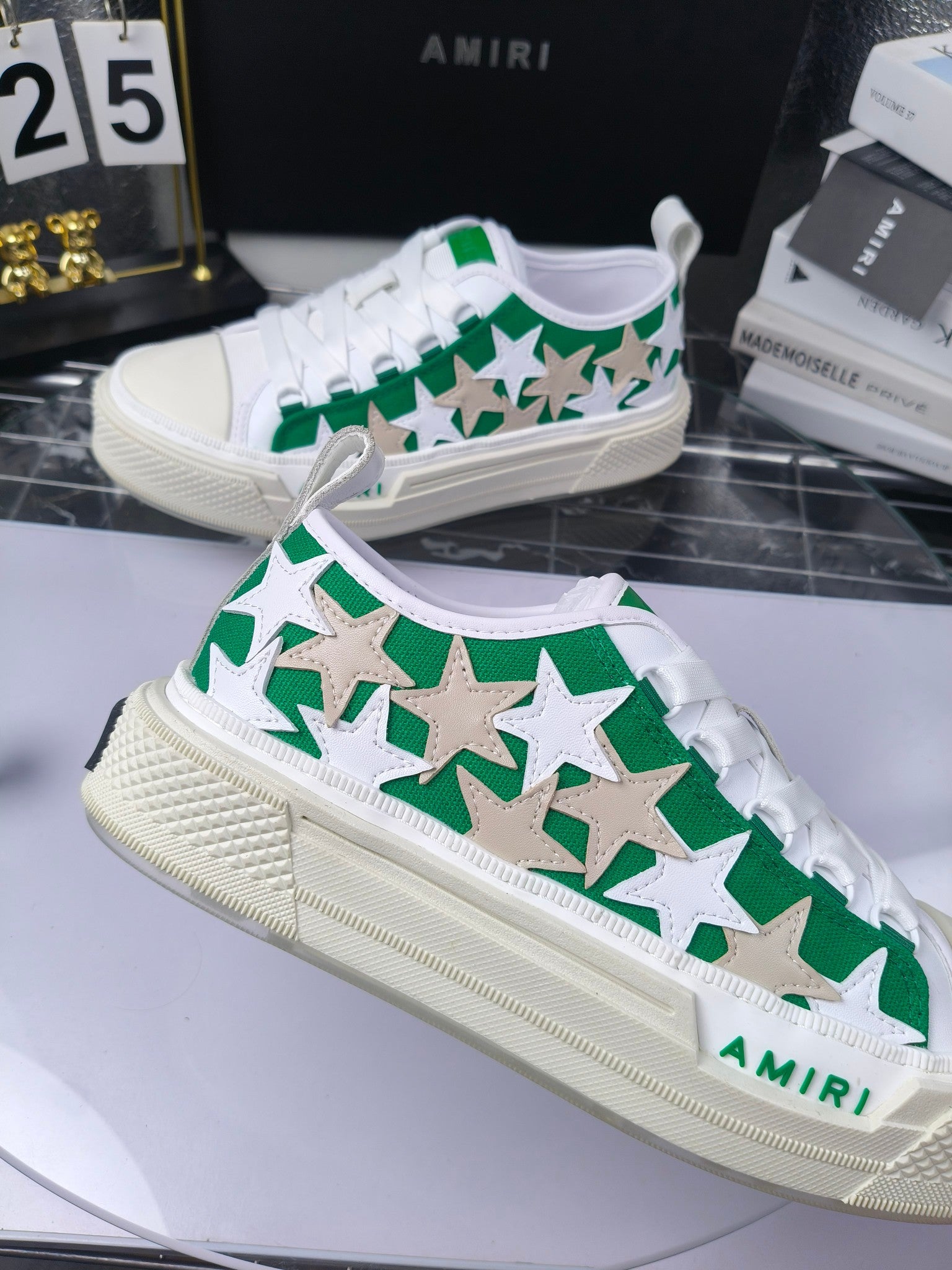 White low-top sneakers with green star pattern, white laces, Amiri branding, angled view