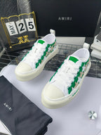 White low-top sneakers with green star motif and white laces, Amiri branding, pair view