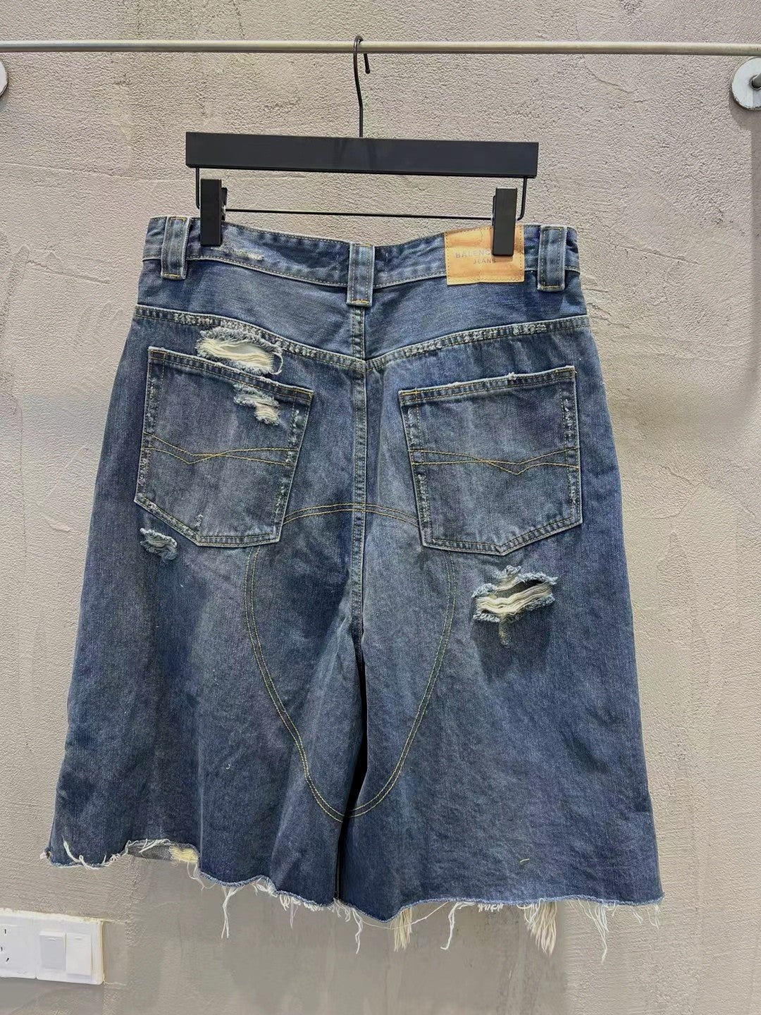 Blue denim shorts with multiple distressed patches and frayed hem, belt loops