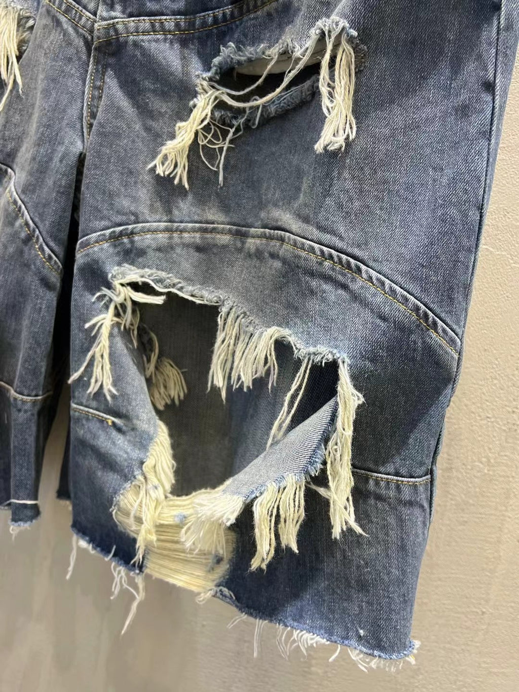 Close-up of distressed blue denim shorts with oversized ripped patch and frayed edges