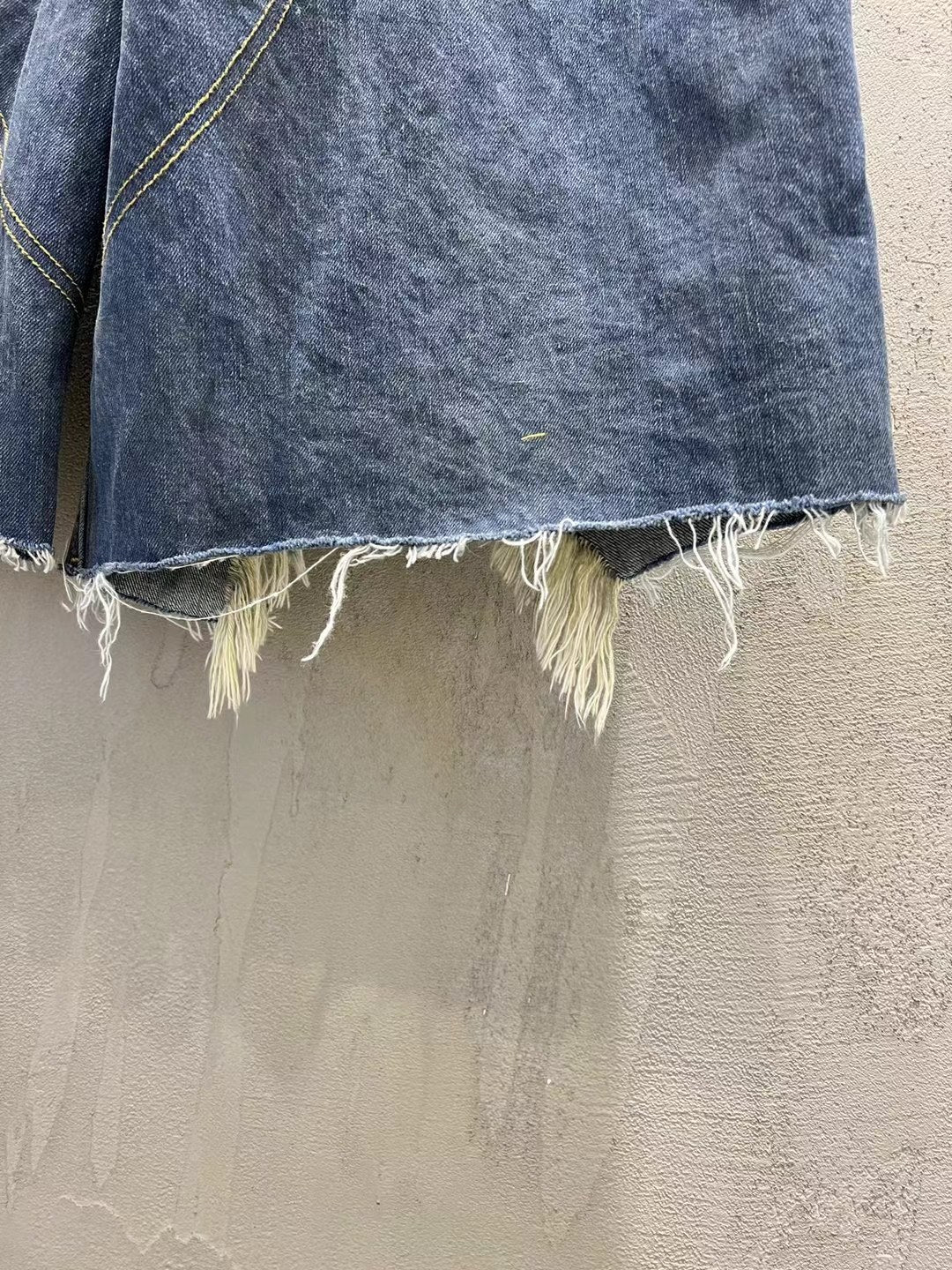 Hem detail of blue denim shorts with raw frayed edge