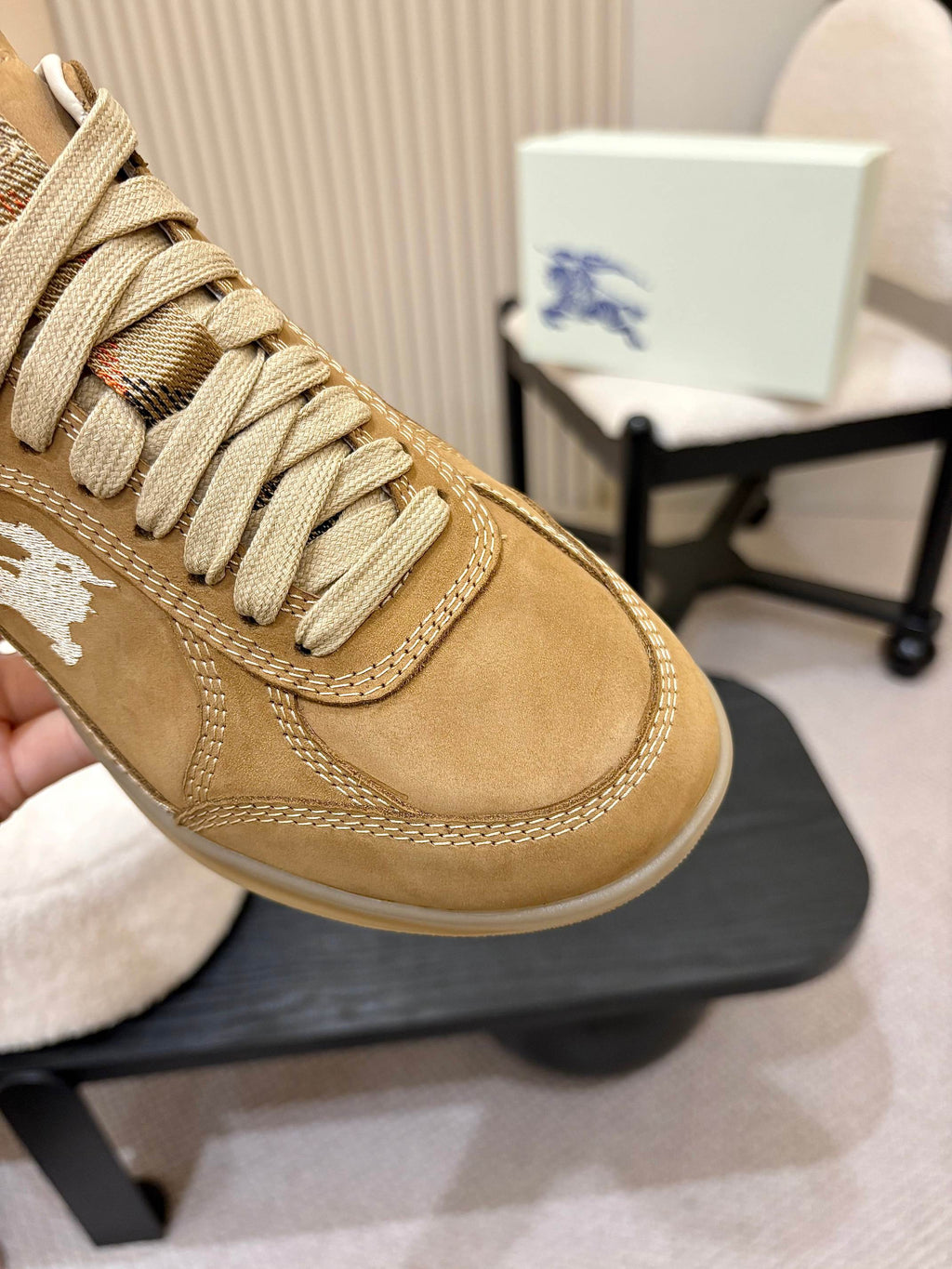 Close-up of tan suede sneaker upper with white horse logo and stitched lacing