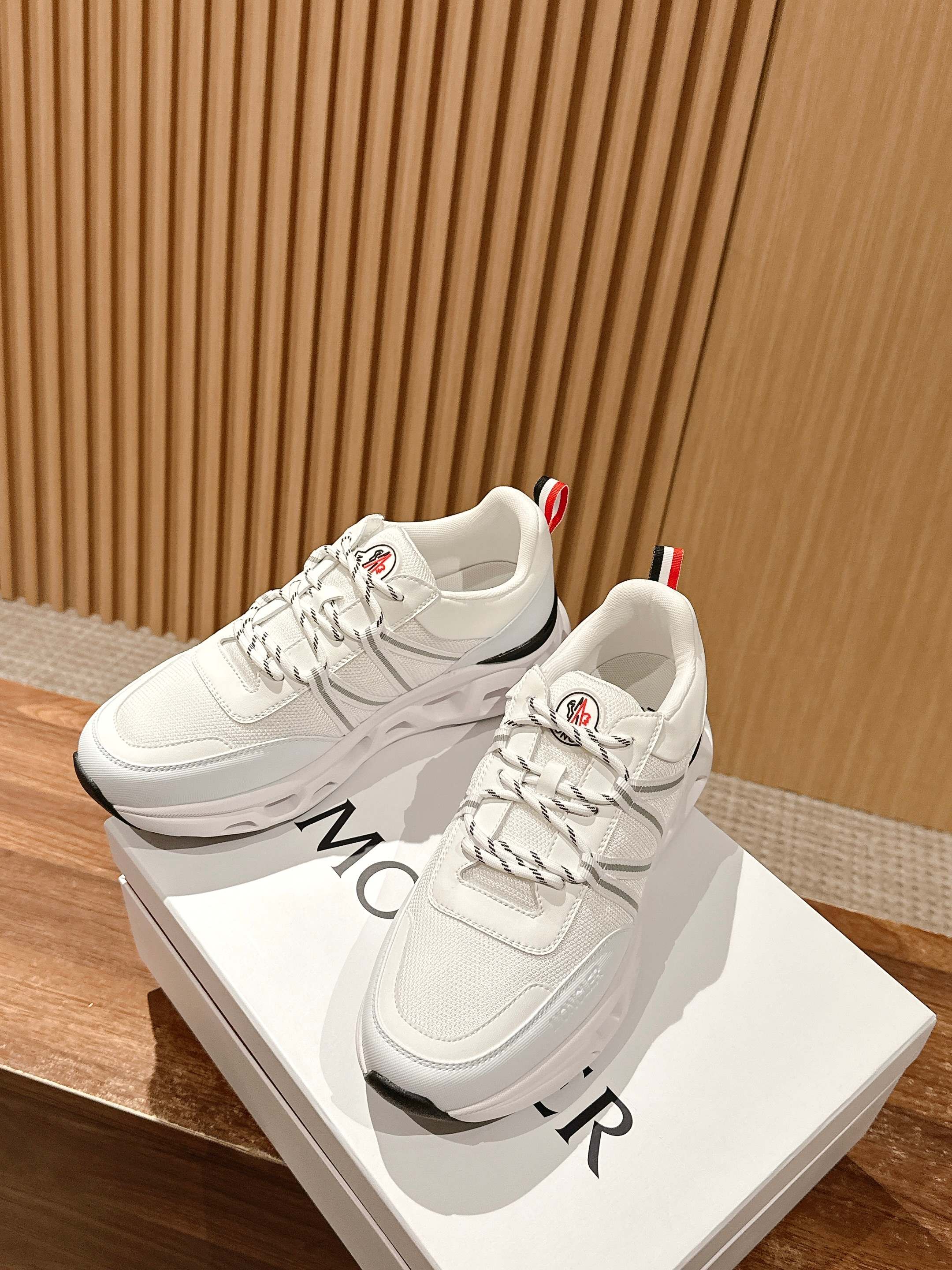 White Moncler sneakers with stitched panels and lace-up front, shown at an angle.