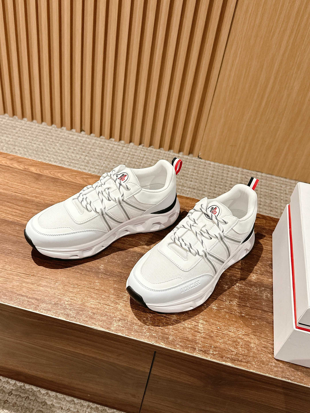 Pair of white Moncler low-top sneakers with ribbed side stripes and red heel tab.