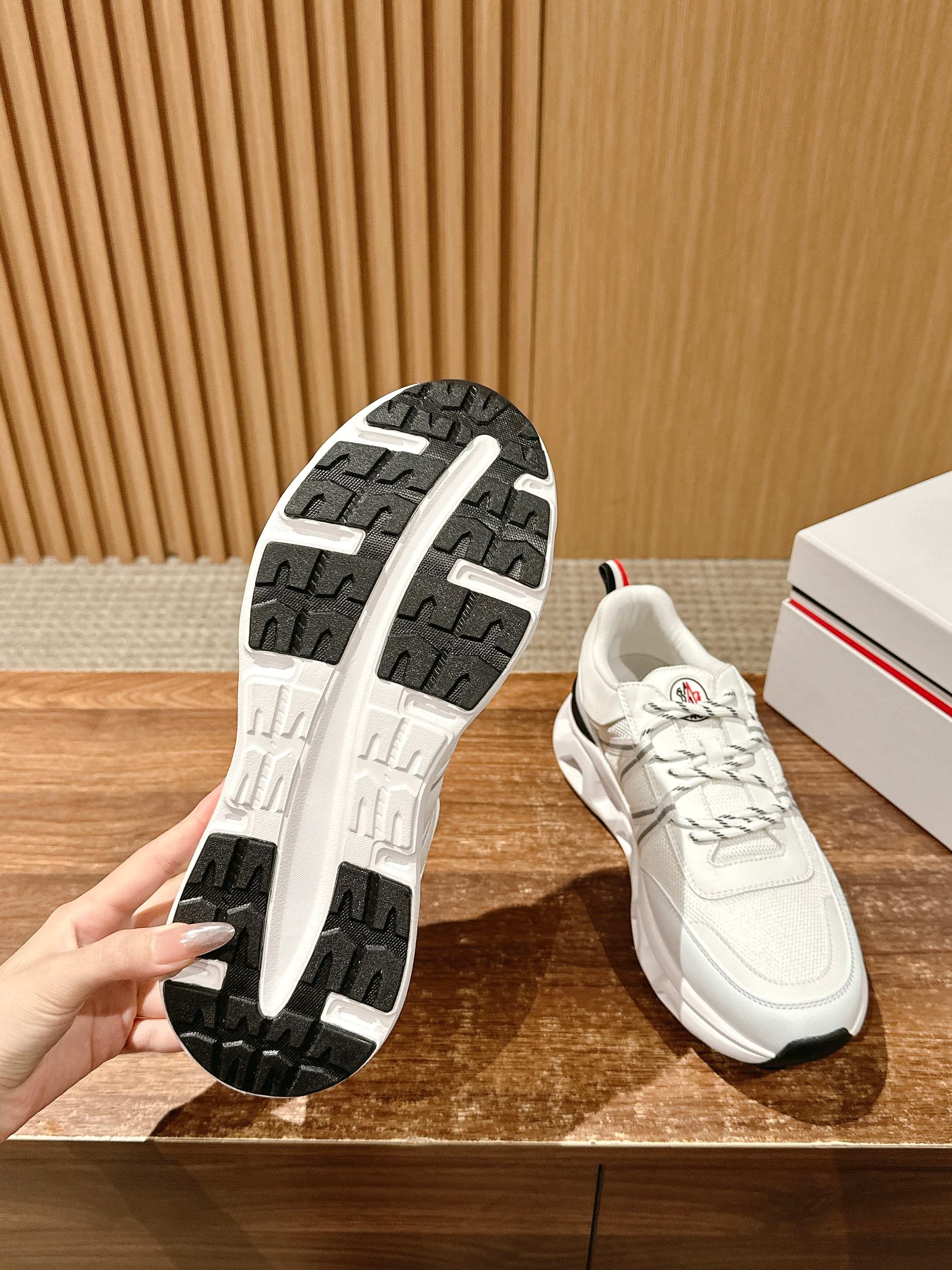 Moncler sneaker outsole with tread pattern and white upper with lace-up details.