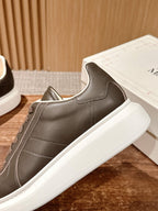 Gray low-top sneaker with brown laces, white sole, and curved side panels