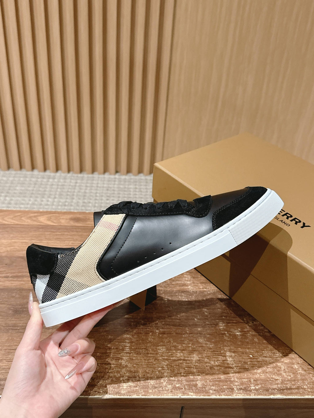 Black sneakers with beige checkered side panel and white sole, hand holding.