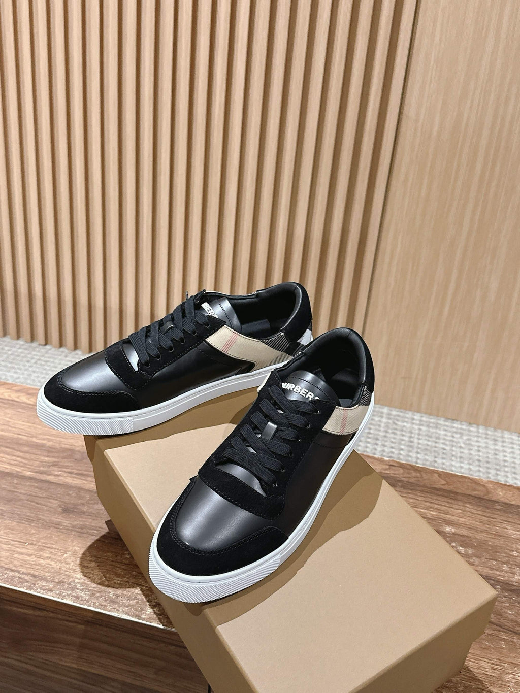 Black lace-up sneakers with white midsole, posed on beige boxes, two-shoe view.