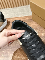 Black sneaker tongue with 'BURBERRY' lettering and lace-up front, close-up.