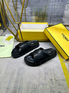 Black slide sandals pair with crisscross straps on yellow display boxes