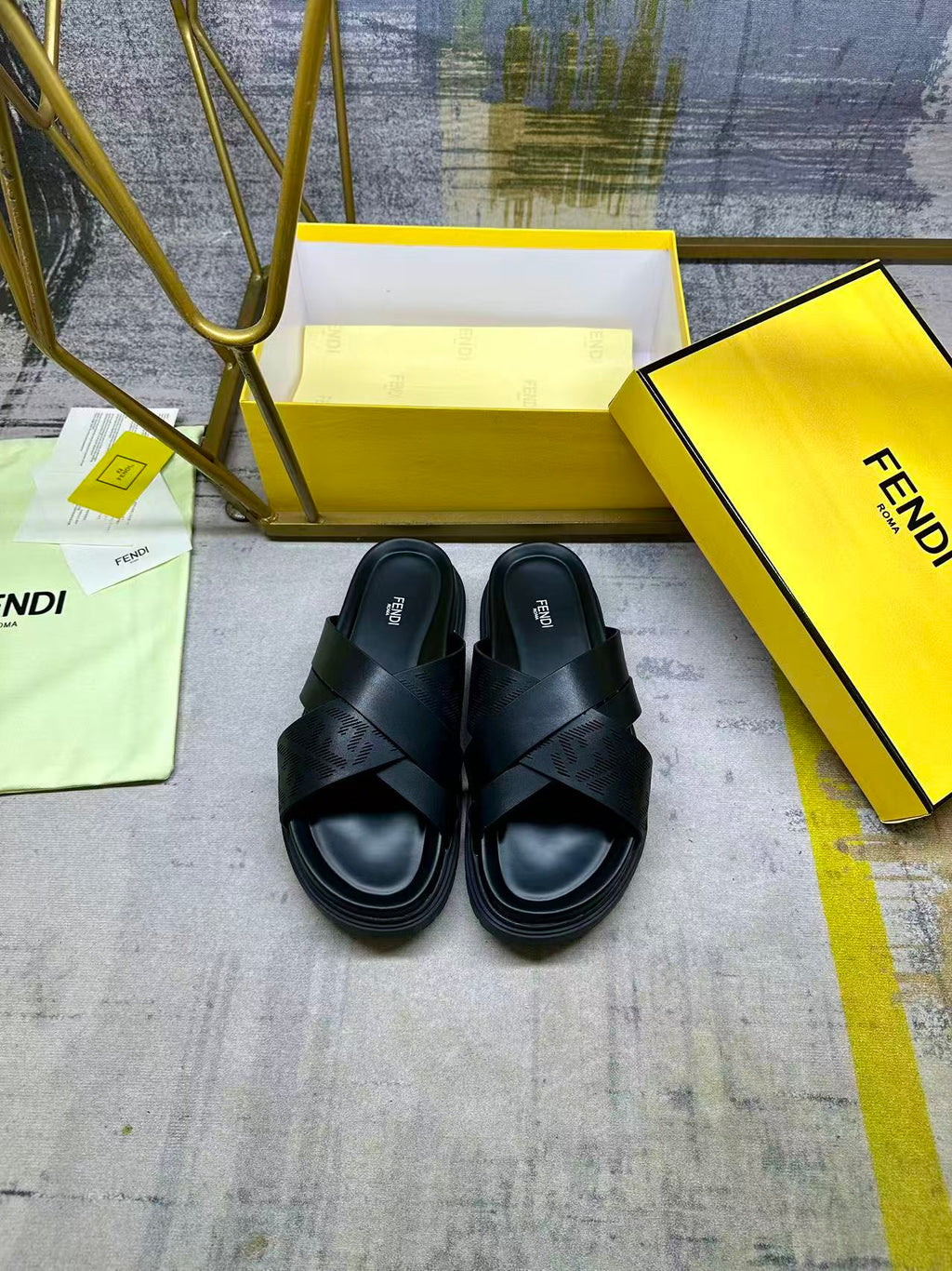 Black slide sandals with wide X straps and open toe on yellow box