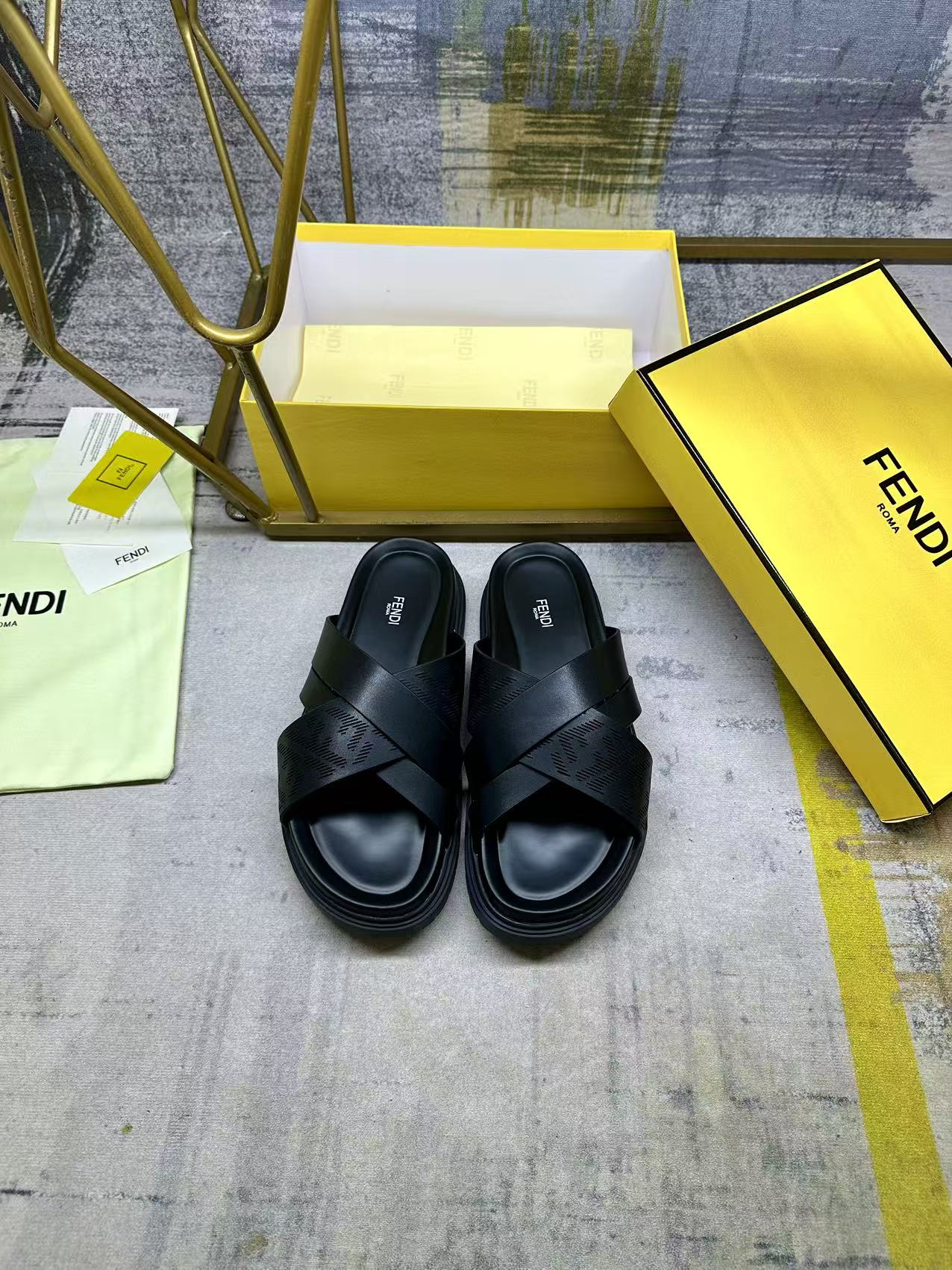 Black slide sandals with wide X straps and open toe on yellow box