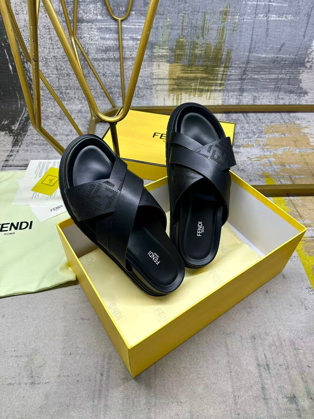 Black slide sandals with wide crossed straps and thick sole on yellow box