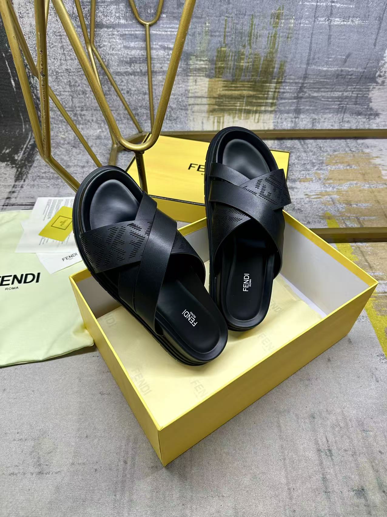Black slide sandals with wide crossed straps and thick sole on yellow box