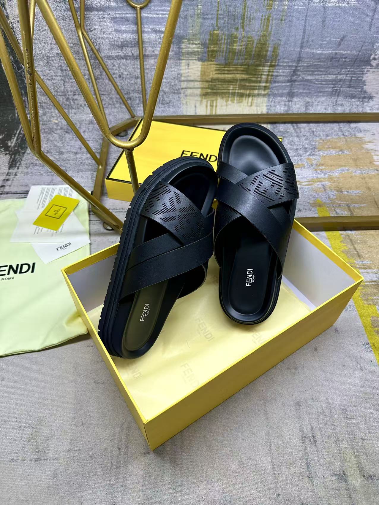 Black slide sandals with wide X straps and thick sole, shown on box