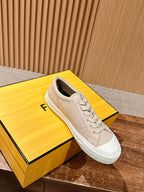 Beige low-top sneakers with lace-up front and white sole, on display box, unisex.