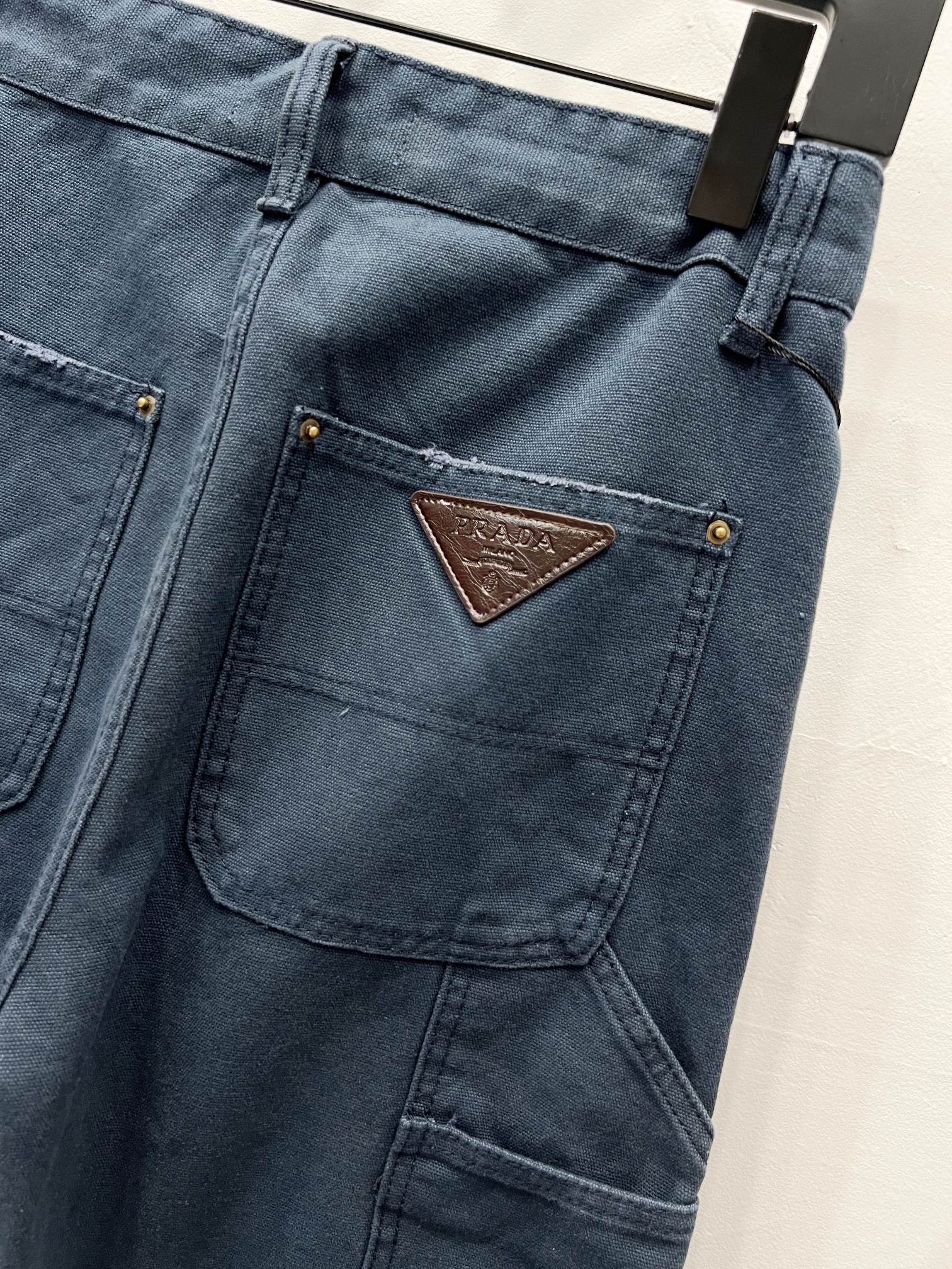 Dark blue denim patch pocket with triangular brown logo and gold button