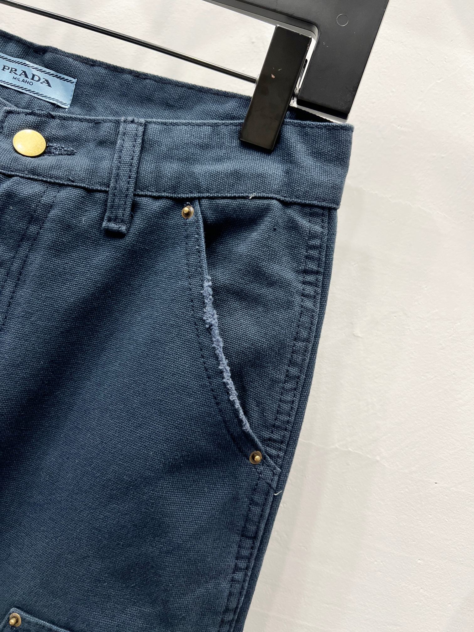 Dark blue denim pants with front closure, gold snap button, and stitched seams