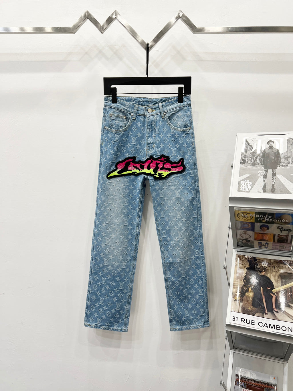 Light blue denim jeans with monogram pattern and colorful graffiti patch on front