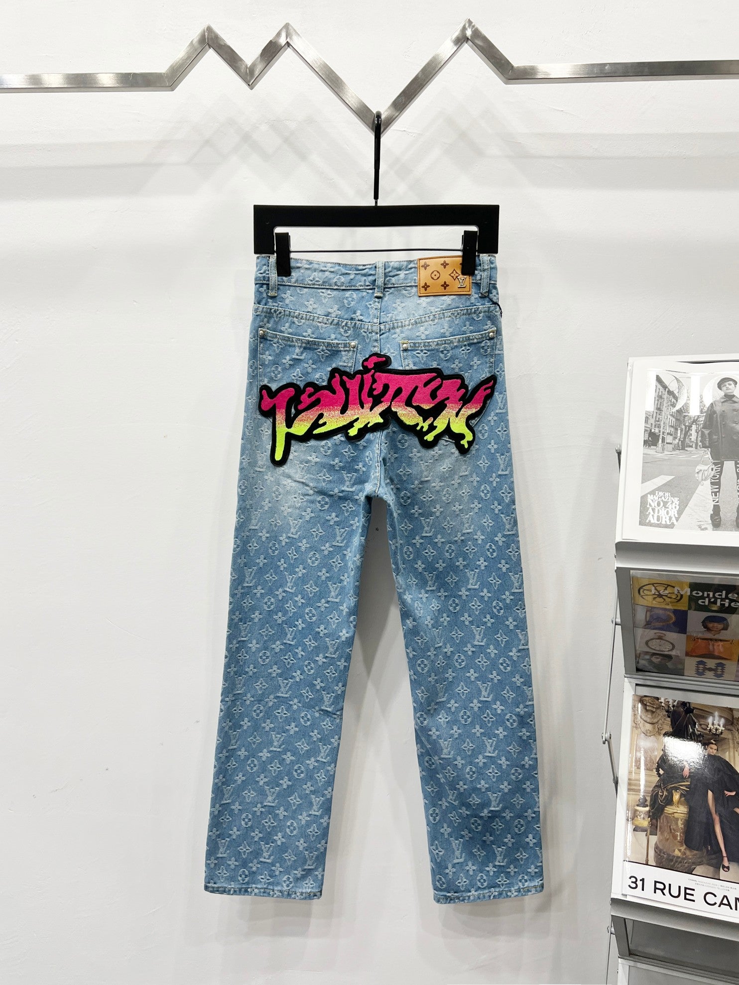 Light blue denim jeans with monogram pattern, graffiti patch across front waistband