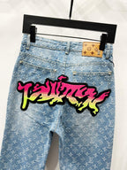 Light blue denim jeans with monogram pattern and large graffiti patch across leg