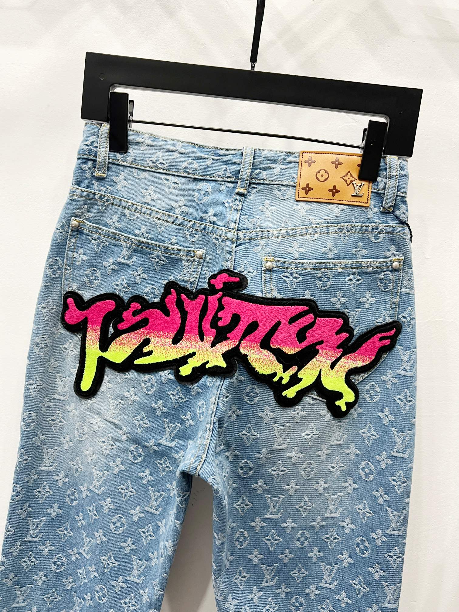 Light blue denim jeans with monogram pattern and large graffiti patch across leg