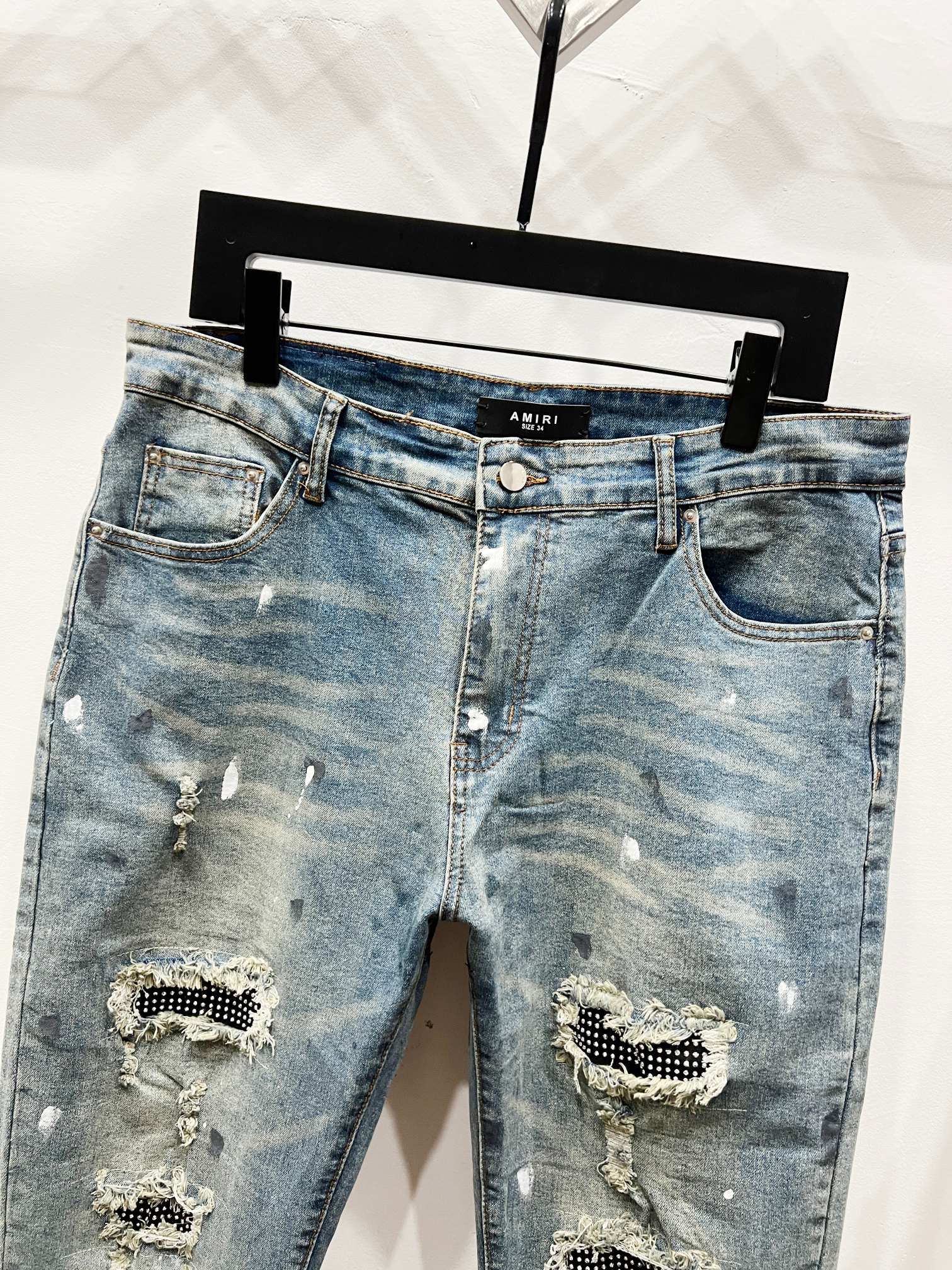 Light blue denim jeans with front rips and studded patch embellishments, mid rise